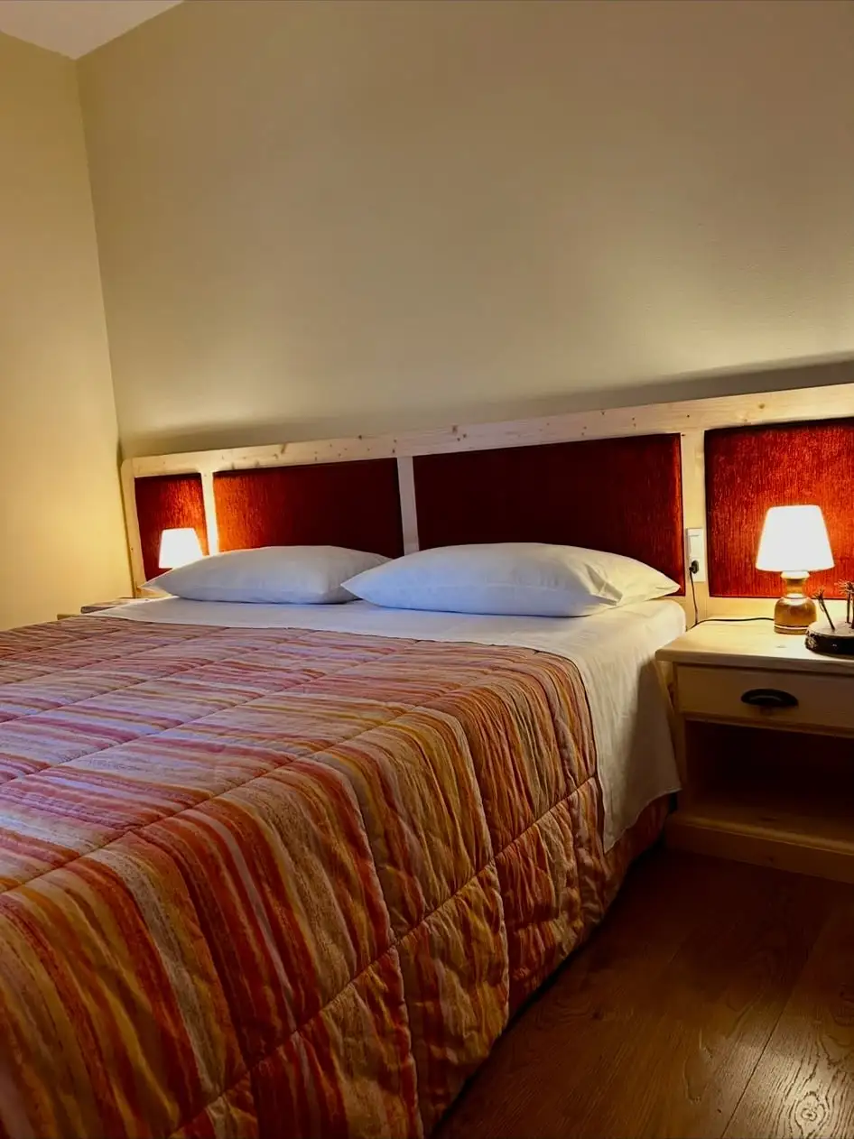 Camera matrimoniale dell’albergo con lampade accese e testata in legno